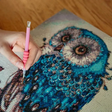 Käsi asettaa timantteja pöllökuvioiseen timanttimaalaukseen – diamond painting -projekti käynnissä.